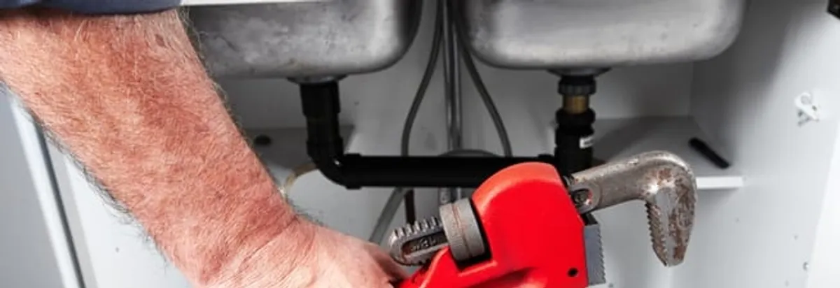 Garbage disposal repair technician tightening drain connections under a kitchen sink in Bellevue, WA